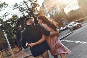 toujours ensemble. vue arrière d'un beau jeune couple se liant et se regardant avec le sourire tout en marchant dans la rue de la ville photo