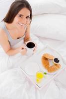 petit déjeuner au lit. vue de dessus d'une belle jeune femme souriante prenant son petit déjeuner au lit et regardant la caméra photo