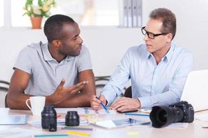 travailler ensemble sur un projet créatif. deux hommes d'affaires confiants en vêtements décontractés assis ensemble à la table et discutant de quelque chose photo