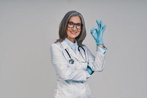 mature belle femme médecin mettant des gants chirurgicaux et souriant photo