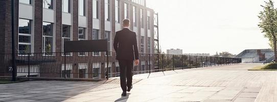 vue arrière sur toute la longueur de l'homme en costume complet marchant près de l'immeuble de bureaux à l'extérieur photo