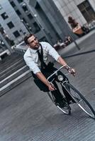 ludique et fonctionnel. beau jeune homme en costume complet avec impatience tout en faisant du vélo à l'extérieur photo