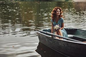 fille charmante. belle jeune femme en robe élégante regardant loin et souriant alors qu'il était assis dans le bateau photo