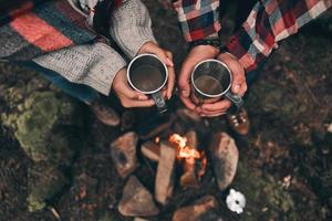 voyage romantique. vue de dessus en gros plan d'un jeune couple tenant des tasses tout en se réchauffant près du feu de camp photo