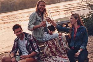 groupe de jeunes en tenue décontractée souriant et portant un toast tout en profitant d'une fête sur la plage près du lac photo