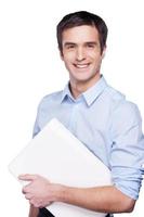 homme d'affaires avec ordinateur portable. beau jeune homme en chemise bleue tenant un ordinateur portable et souriant debout isolé sur blanc photo