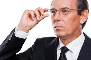 réfléchir à des solutions. portrait d'un homme mûr réfléchi en tenues de soirée ajustant ses lunettes et regardant ailleurs en se tenant debout sur fond blanc photo