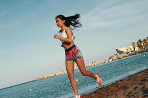 chaque jour rempli de sport. jolie jeune femme en vêtements de sport jogging tout en faisant de l'exercice à l'extérieur photo