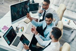 pleine concentration au travail. vue de dessus de jeunes hommes modernes en tenues de soirée analysant les données boursières tout en travaillant au bureau photo