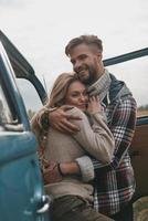 tout simplement amoureux. beau jeune couple embrassant et souriant tout en se tenant à l'extérieur près de la mini-fourgonnette de style rétro photo