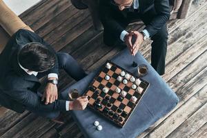 jouer aux échecs. vue de dessus de jeunes hommes réfléchis en costume complet jouant aux échecs assis à l'intérieur photo