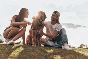 chanceux d'être ensemble. jeune couple moderne assis sur l'herbe avec leur chien tout en passant du temps libre dans le parc photo