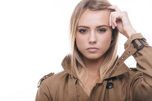 belle. jolie jeune femme en manteau ajustant ses cheveux et regardant la caméra en se tenant debout sur fond blanc photo