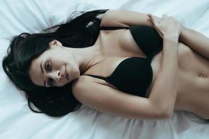 beauté naturelle. vue de dessus de la belle jeune femme en soutien-gorge noir sexy posant de manière séduisante en position allongée sur le lit à la maison photo