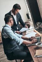 donner des conseils commerciaux. deux jeunes hommes modernes en tenues de soirée travaillant ensemble assis à l'intérieur photo