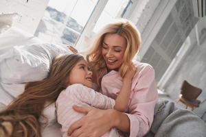 vue de dessus de la belle jeune mère avec sa jolie petite fille souriante et embrassant en position couchée sur le lit à la maison photo