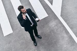 s'occuper des affaires. vue de dessus pleine longueur d'un jeune homme en costume complet parlant au téléphone tout en se tenant à l'extérieur photo