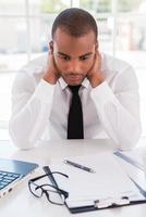 malade et fatigué. jeune homme africain déprimé en tenues de soirée tenant la tête dans les mains alors qu'il était assis sur son lieu de travail photo