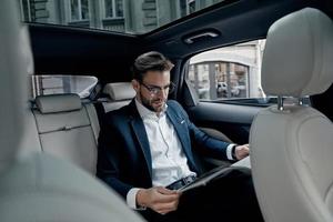 lire les dernières nouvelles. beau jeune homme en costume complet lisant un journal assis dans la voiture photo