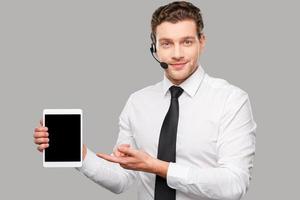 copier l'espace sur son ordinateur portable. beau jeune homme en tenues de soirée et casque pointant une tablette numérique en se tenant debout sur fond gris photo