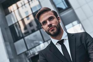 perdu dans les pensées. beau jeune homme en costume complet regardant loin tout en se tenant à l'extérieur photo