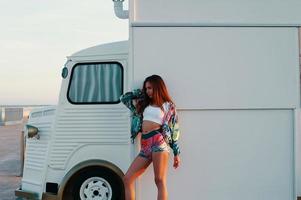 la féminité. jolie jeune femme en vêtements de sport posant debout contre un camion de nourriture à l'extérieur photo