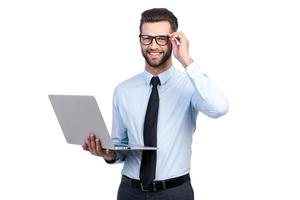 expert en affaires confiant. confiant jeune bel homme en chemise et cravate tenant un ordinateur portable et souriant en se tenant debout sur fond blanc photo