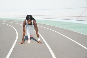 jeune femme africaine concentrée debout à la position de départ sur une piste de course à l'extérieur photo