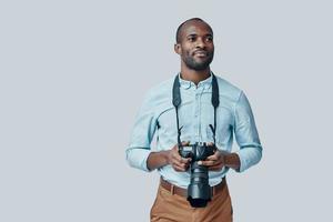 beau jeune homme africain regardant loin et souriant en se tenant debout sur fond gris photo