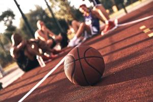 un autre grand jeu. groupe de jeunes hommes en vêtements de sport communiquant assis sur le terrain de basket à l'extérieur photo