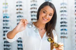 choix difficile. belle jeune femme choisissant des lunettes de soleil en magasin photo