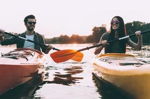 la vie est meilleure sur le fleuve. joyeux jeune couple faisant du kayak sur la rivière avec le coucher du soleil en arrière-plan photo