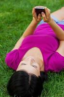 rester en contact avec des amis. séduisante jeune femme tapant un message sur son téléphone portable et souriante en position couchée dans l'herbe photo