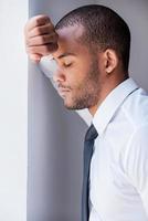 fatigué et surmené. vue latérale d'un jeune homme déprimé en chemise et cravate appuyé contre le mur et gardant les yeux fermés photo