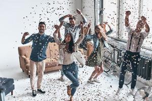 juste se sentir heureux. vue de dessus pleine longueur de jeunes gens heureux gesticulant et souriant tout en dansant avec des confettis volant partout photo