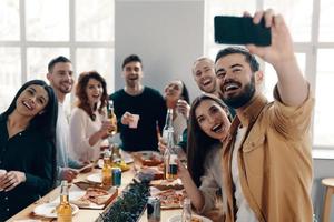 capter l'instant. groupe de jeunes en tenue décontractée prenant un selfie et souriant tout en organisant un dîner à l'intérieur photo