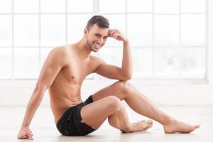 garder le corps en parfaite forme. beau jeune homme musclé assis sur le sol et souriant photo