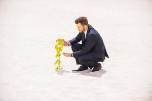 la naissance d'une nouvelle vie. jeune homme confiant en tenues de soirée examinant une plante qui pousse dans le sable photo