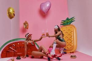 belles jeunes femmes en maillot de bain portant un toast et souriant assis sur fond rose photo