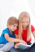 lire son livre préféré. deux enfants mignons lisant un livre ensemble assis ensemble sur le lit photo