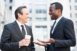 avoir une pause pour discuter. deux hommes d'affaires gais parlant et gesticulant tout en se tenant à l'extérieur photo