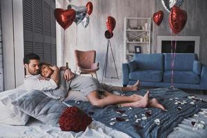 fait pour s'aimer. beau jeune couple embrassant et souriant en position couchée sur le lit à la maison photo