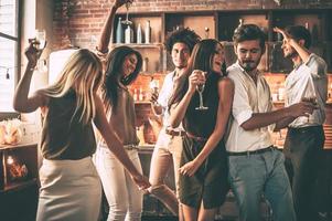 jouer dur. jeunes joyeux dansant et buvant tout en profitant d'une fête à la maison dans la cuisine photo