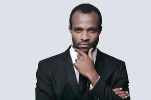 bel entrepreneur. portrait d'un jeune homme africain confiant tenant la main sur le menton et regardant la caméra en se tenant debout sur fond gris photo