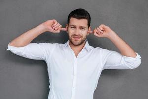 son trop fort frustré jeune homme couvrant les oreilles avec les mains et regardant la caméra en se tenant debout sur fond gris photo