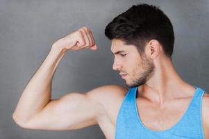 montrant son biceps parfait. confiant jeune homme musclé posant debout sur fond gris photo