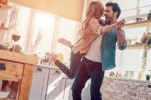 tellement génial d'être ensemble sur toute la longueur d'un beau jeune couple en vêtements décontractés dansant et souriant tout en se tenant dans la cuisine à la maison photo