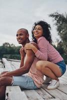 joie simple d'aimer. heureux jeune couple embrassant et souriant assis sur la jetée près du lac photo