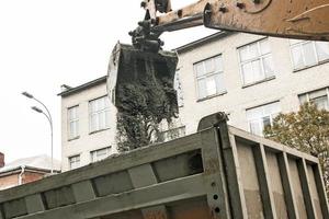 travaux routiers dans la rue de la ville. le godet de la pelle récupère l'ancien revêtement et le charge dans un camion à benne basculante photo