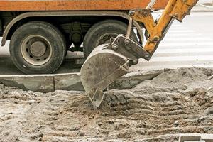 travaux routiers dans la rue de la ville. le godet de la pelle récupère l'ancien revêtement et le charge dans un camion à benne basculante photo